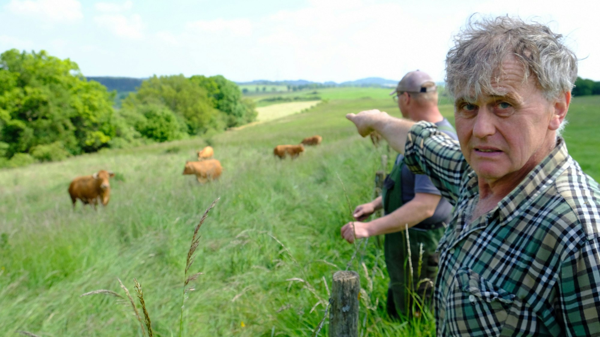 Der Landwirt Paul Milz deutet mit ausgestrecktem Arm auf die Weide, wo einige seiner Rinder stehen. Sein Kollege Marcel May steht neben ihm.