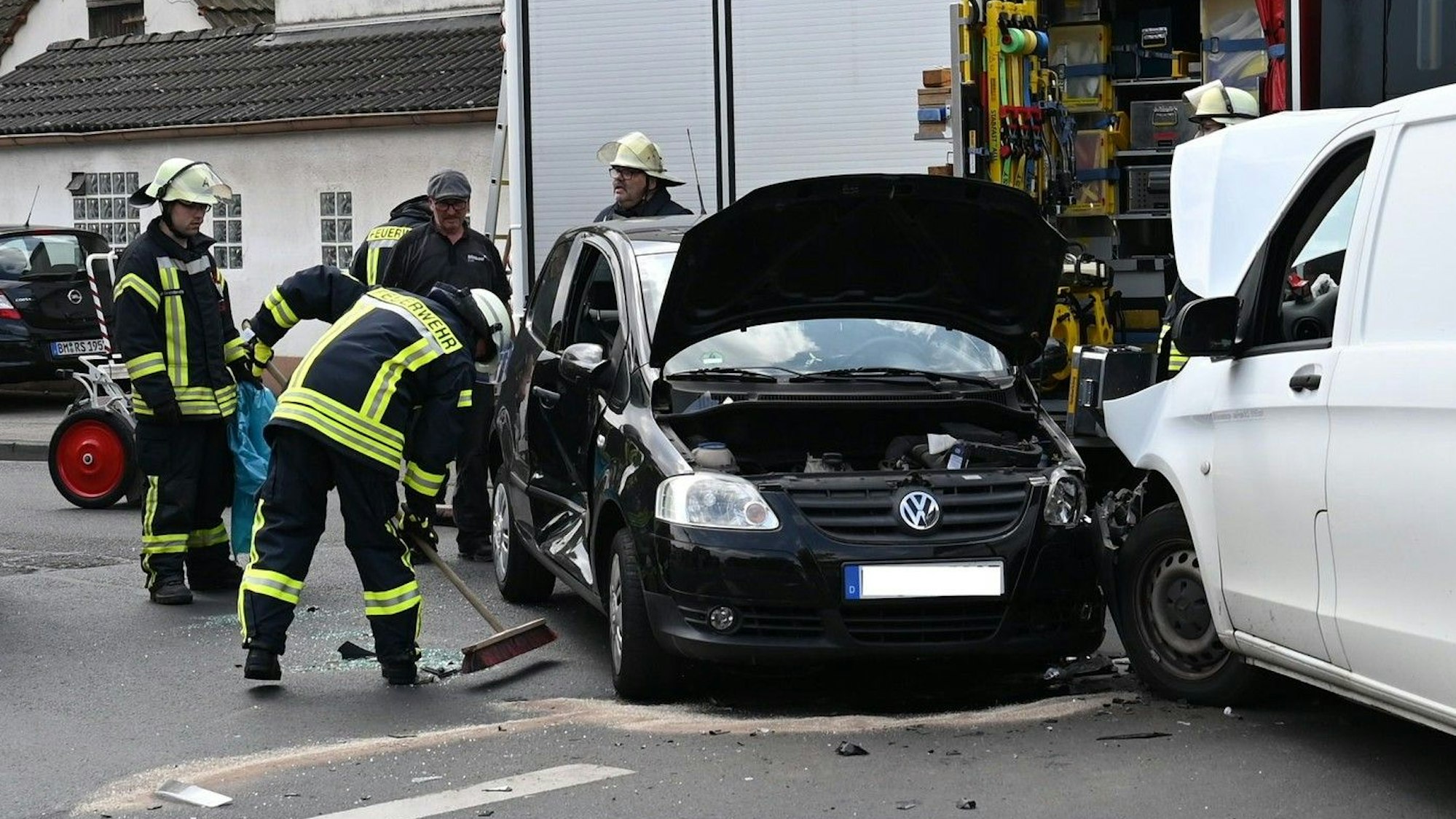 Das Bild zeigt zwei Autos die zusammengestoßen sind und Feuerwehrmänner, die auslaufende Flüssigkeiten abstreuen.