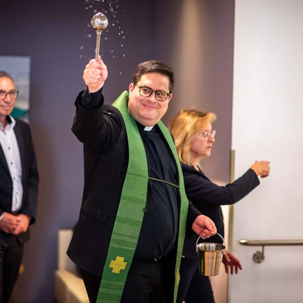 Das Bild zeigt unter anderem Pfarrer Tobias Hopmann, der Weihwasser im Raum verteilt.