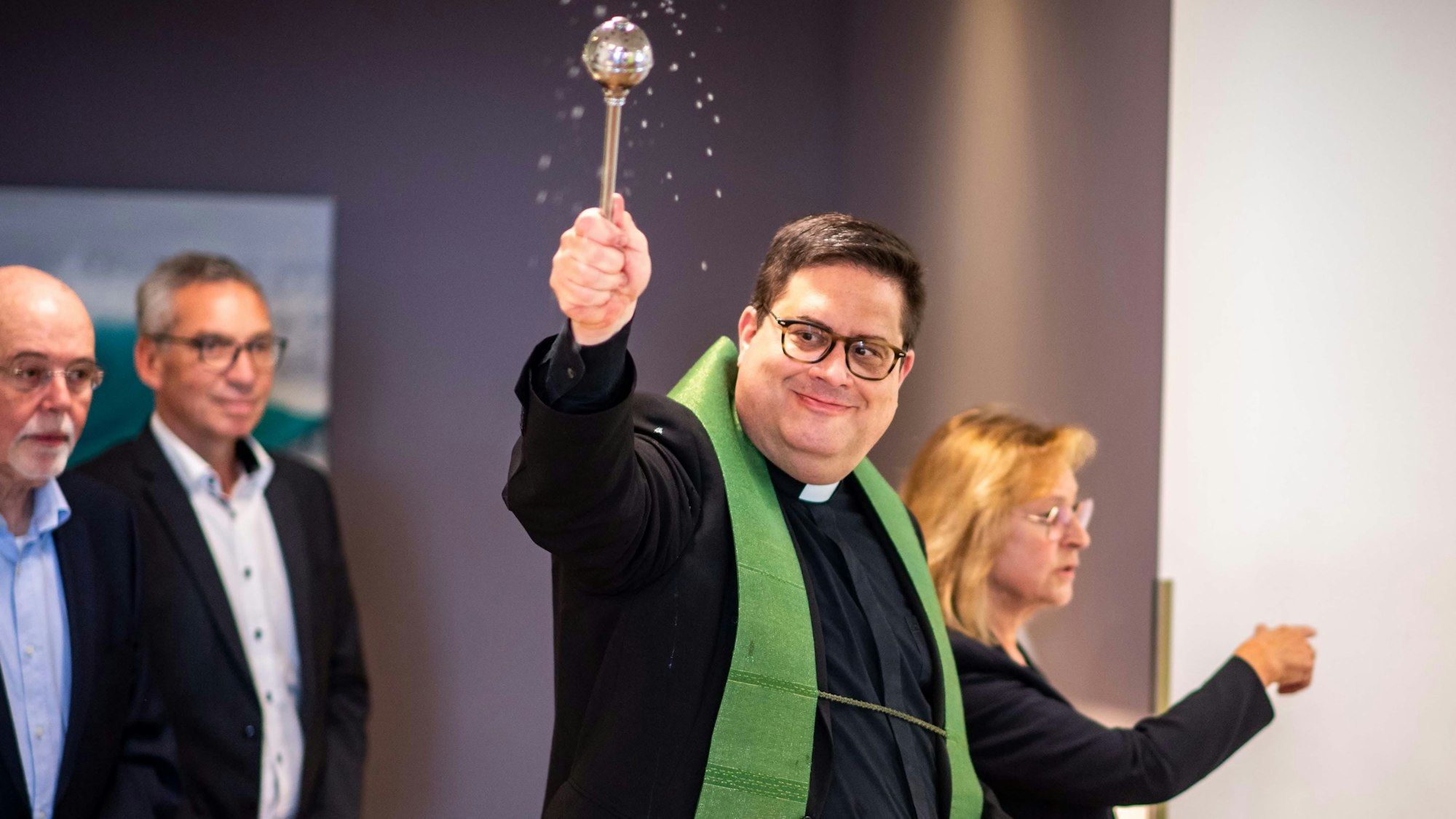Das Bild zeigt unter anderem Pfarrer Tobias Hopmann, der Weihwasser im Raum verteilt.