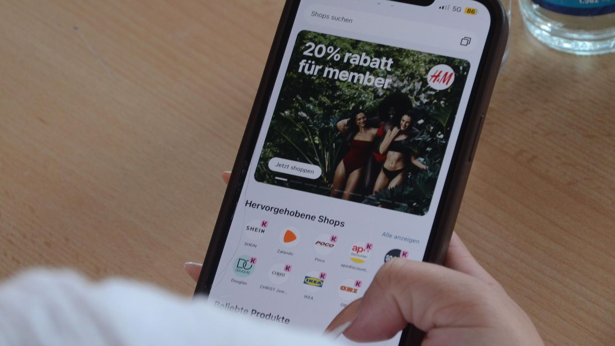 Eine Hand mit langen künstlichen Fingernägeln hält ein Smartphone. Sie hat eine Seite für Online-Shopping geöffnet.