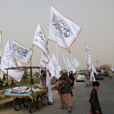 Ein afghanischer Mann und Kinder verkaufen während einer Feier zum zweiten Jahrestag des Abzugs der US-amerikanischen Truppen aus Afghanistan Taliban-Fahnen an Passanten.