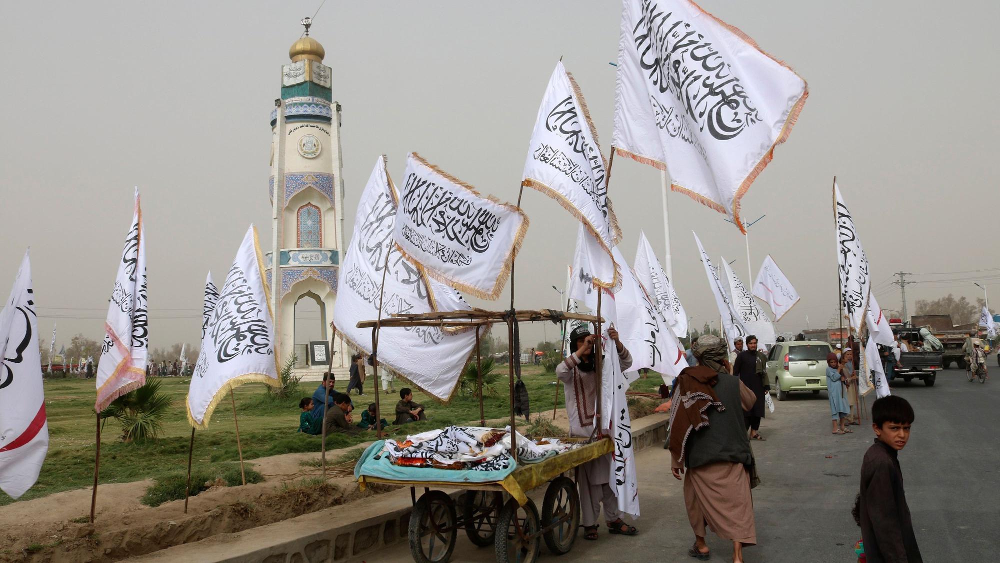 Ein afghanischer Mann und Kinder verkaufen während einer Feier zum zweiten Jahrestag des Abzugs der US-amerikanischen Truppen aus Afghanistan Taliban-Fahnen an Passanten.