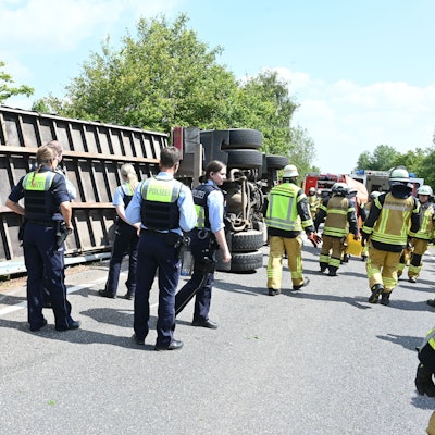 Ein Lkw mit einem Container-Anhänger ist bei Kall umgekippt. Zahlreiche Polizisten und Feuerwehrleute stehen an der Unfallstelle.