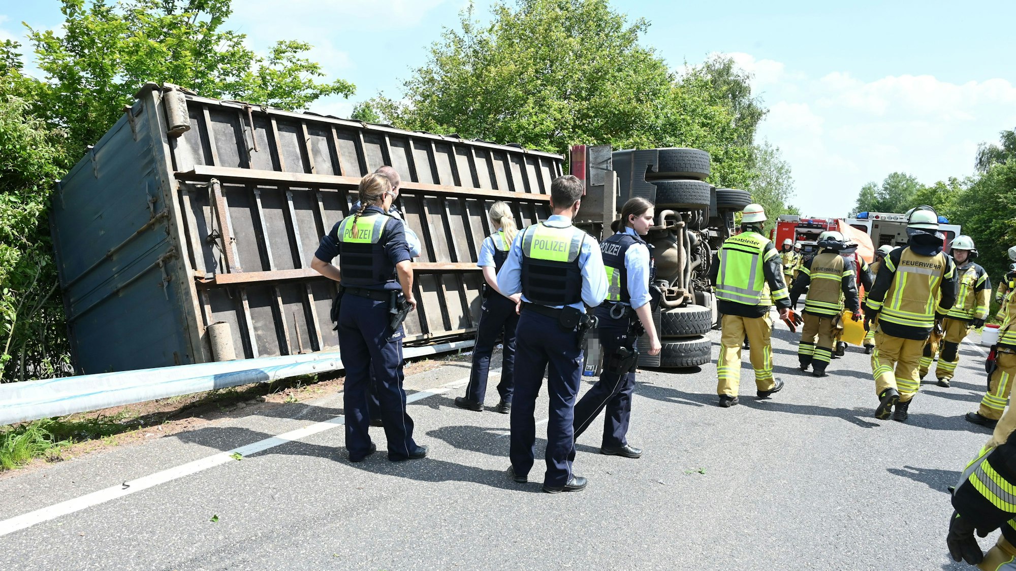 Ein Lkw mit einem Container-Anhänger ist bei Kall umgekippt. Zahlreiche Polizisten und Feuerwehrleute stehen an der Unfallstelle.