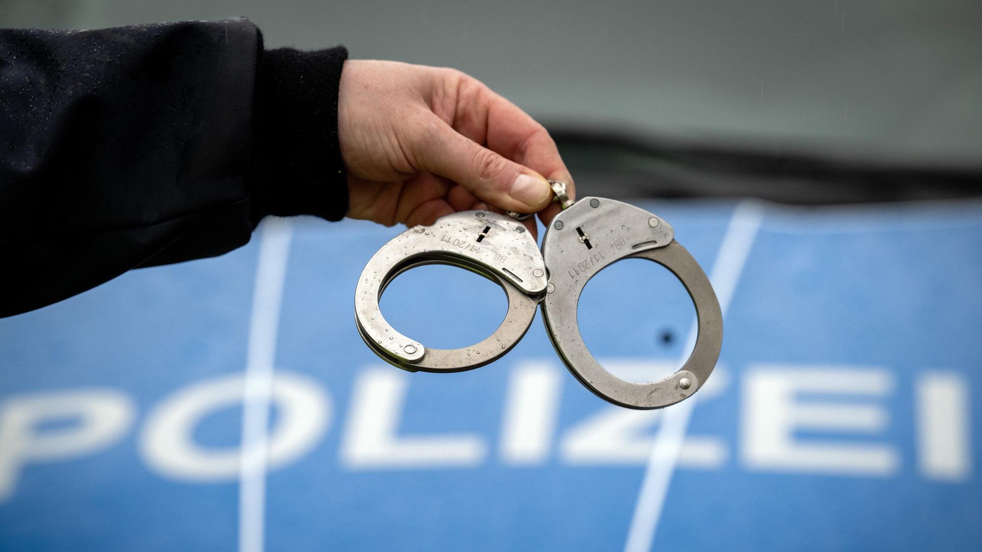 Ein Polizist hält ein Paar Handschellen vor der Motorhaube eines Polizeiwagens.