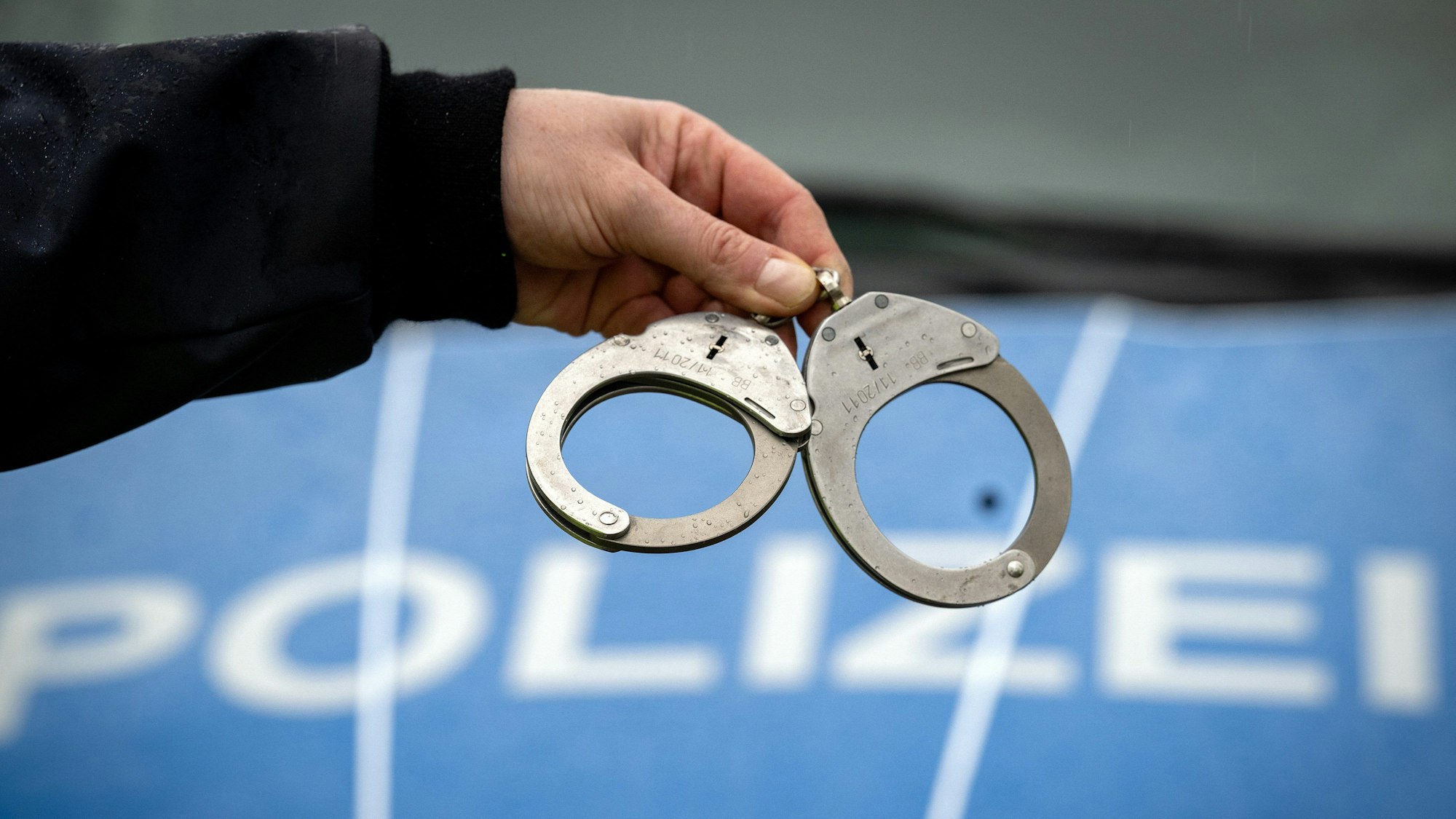 Ein Polizist hält ein Paar Handschellen vor der Motorhaube eines Polizeiwagens.