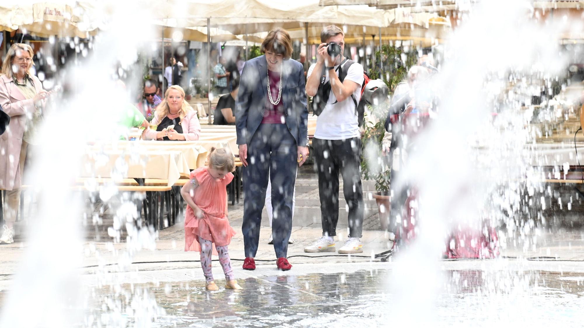OB Reker und ein kleines Mädchen spielen am Brunnen.