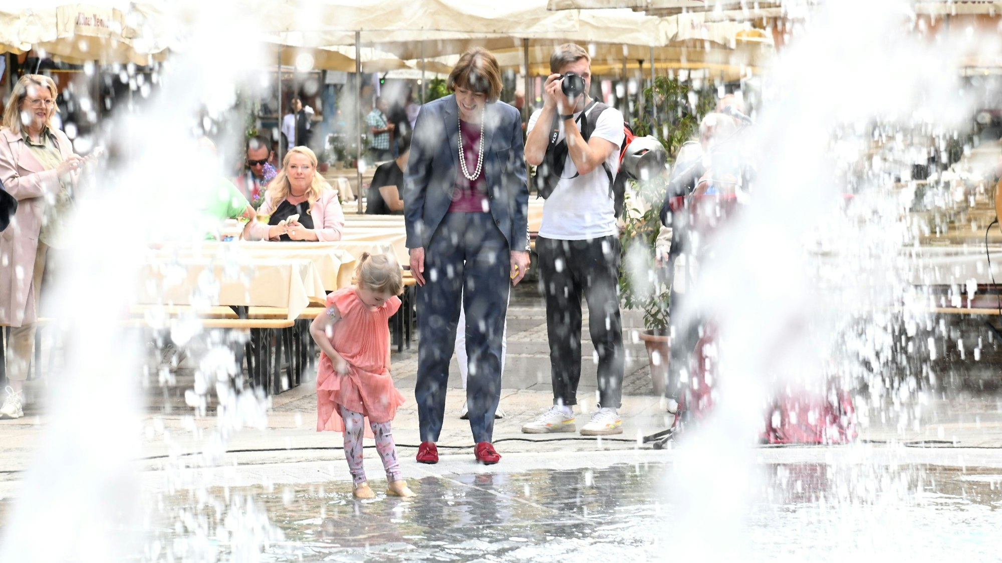 OB Reker und ein kleines Mädchen spielen am Brunnen.