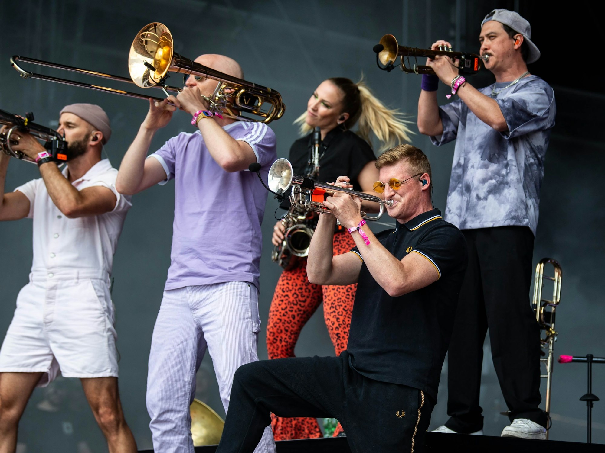 Bunt angezogenen Musikerinnen und Musiker der Band Querbeat stehen auf einer Bühne und spielen Posaune, Trompete und Saxophon.