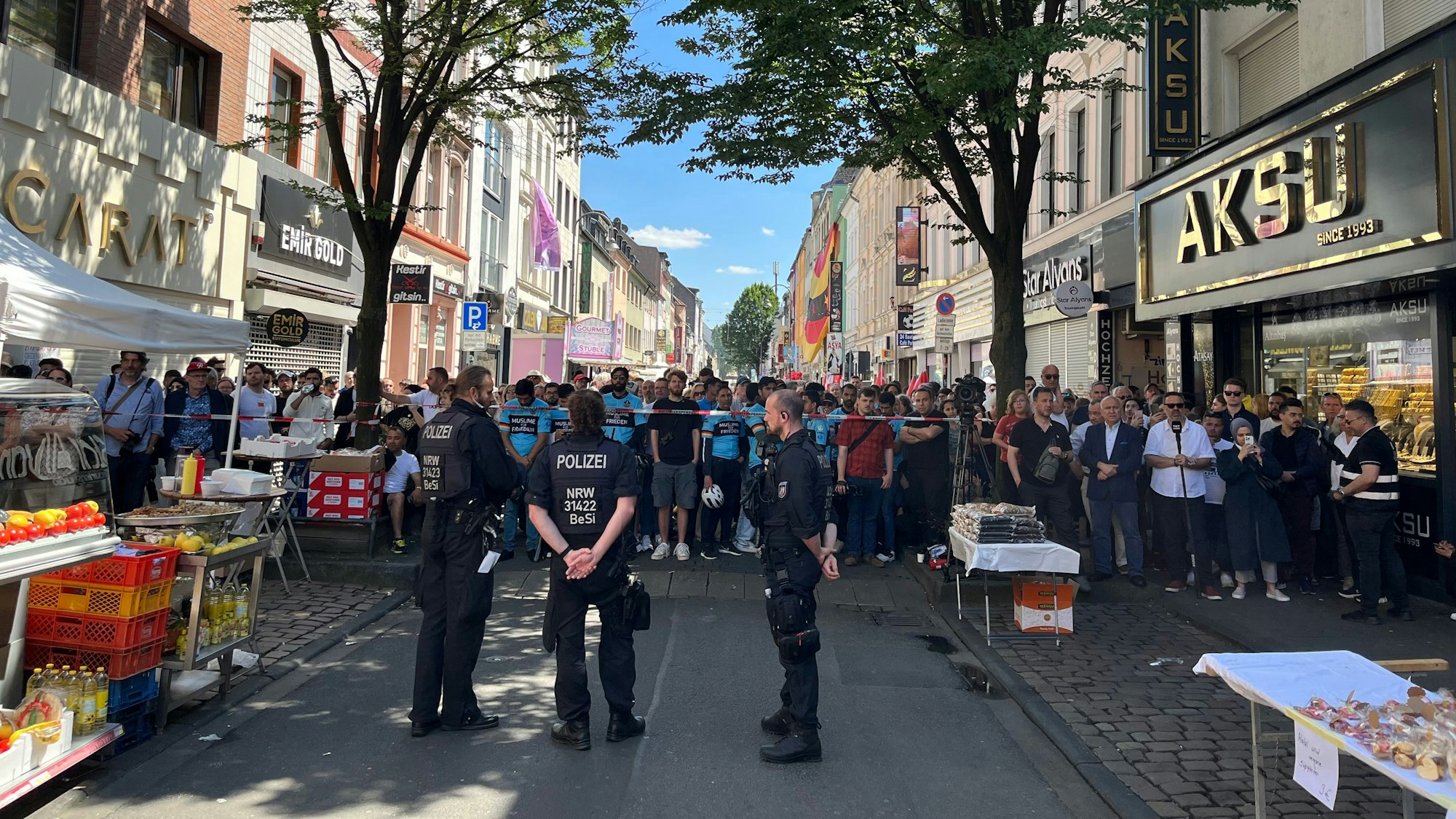 Besucher des Birlikte-Gedenkfestes warten vor einer Absprerrung auf der Keupstraße.