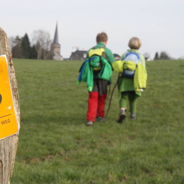 Zwei Kinder wandern auf dem Bergischen Weg in Richtung der Kirche von Neunkirchen.