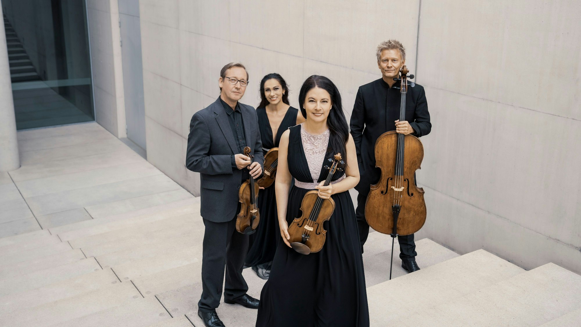 Das vierköpfige Minguet Quartett posiert mit Streichinstrumenten in einem Treppenhaus.