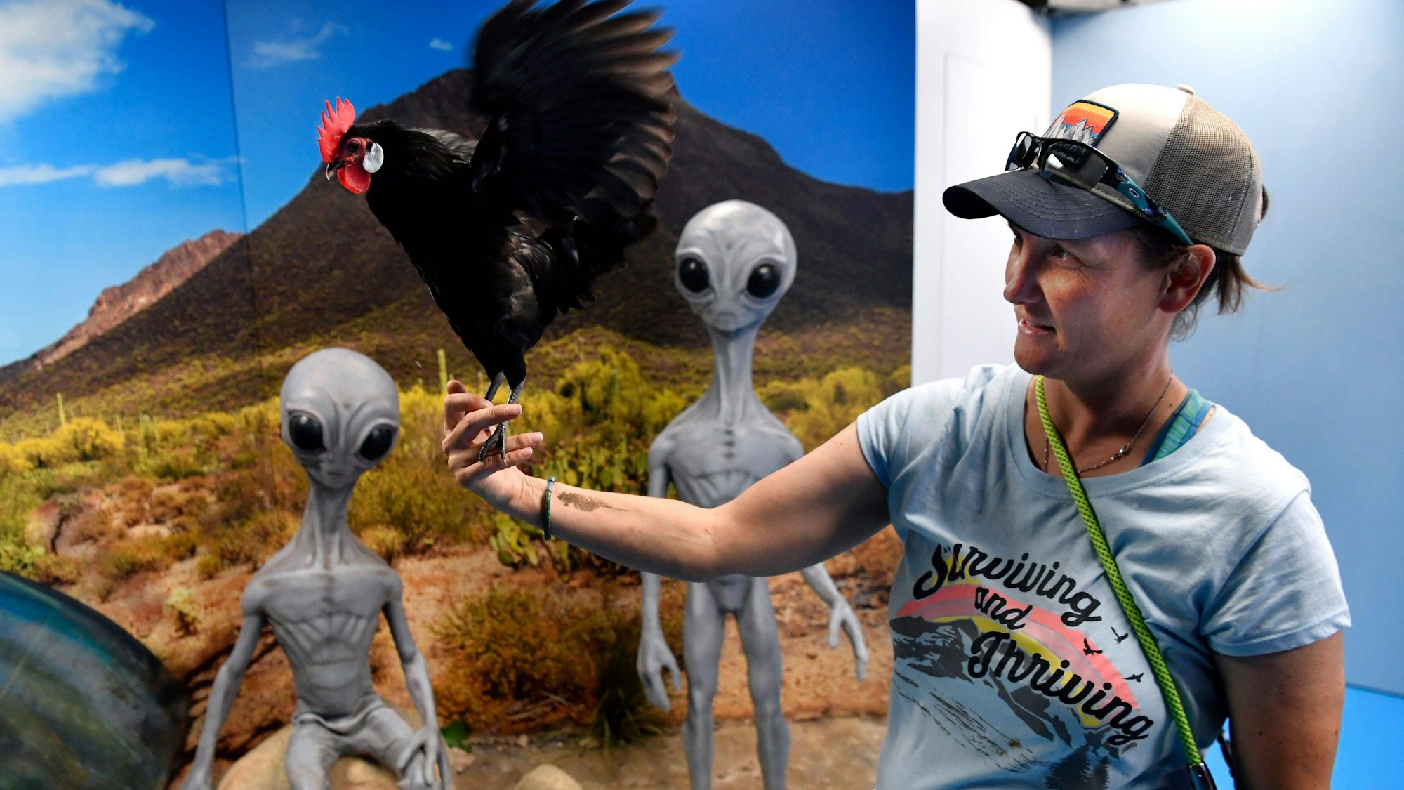 Eine Frau hält vor einem Alien-Plakat einen Hahn auf der Hand.