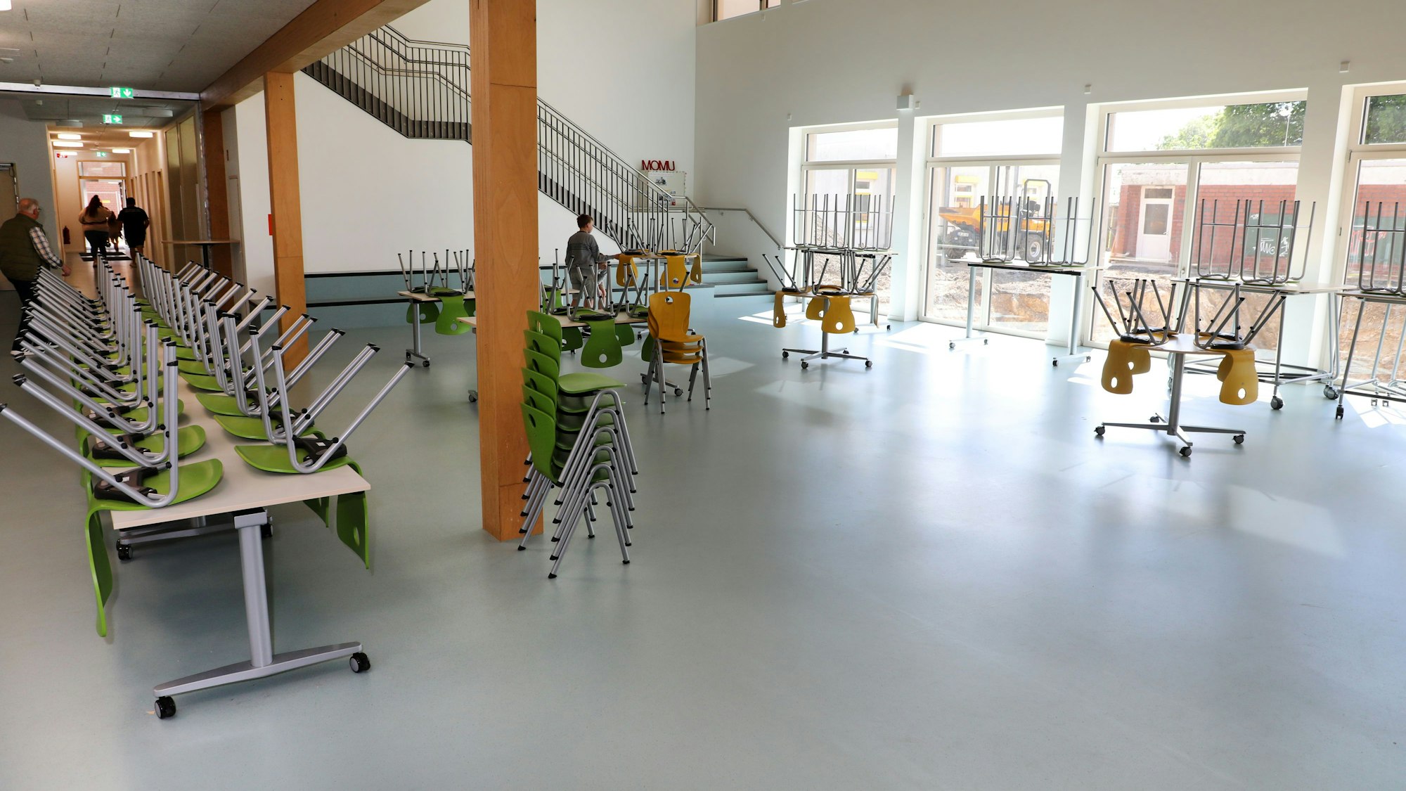 Blick in einen großen Raum mit Tischen auf denen Stühle hochgestellt sind. Durch die Fenster fällt Sonne in den Raum.