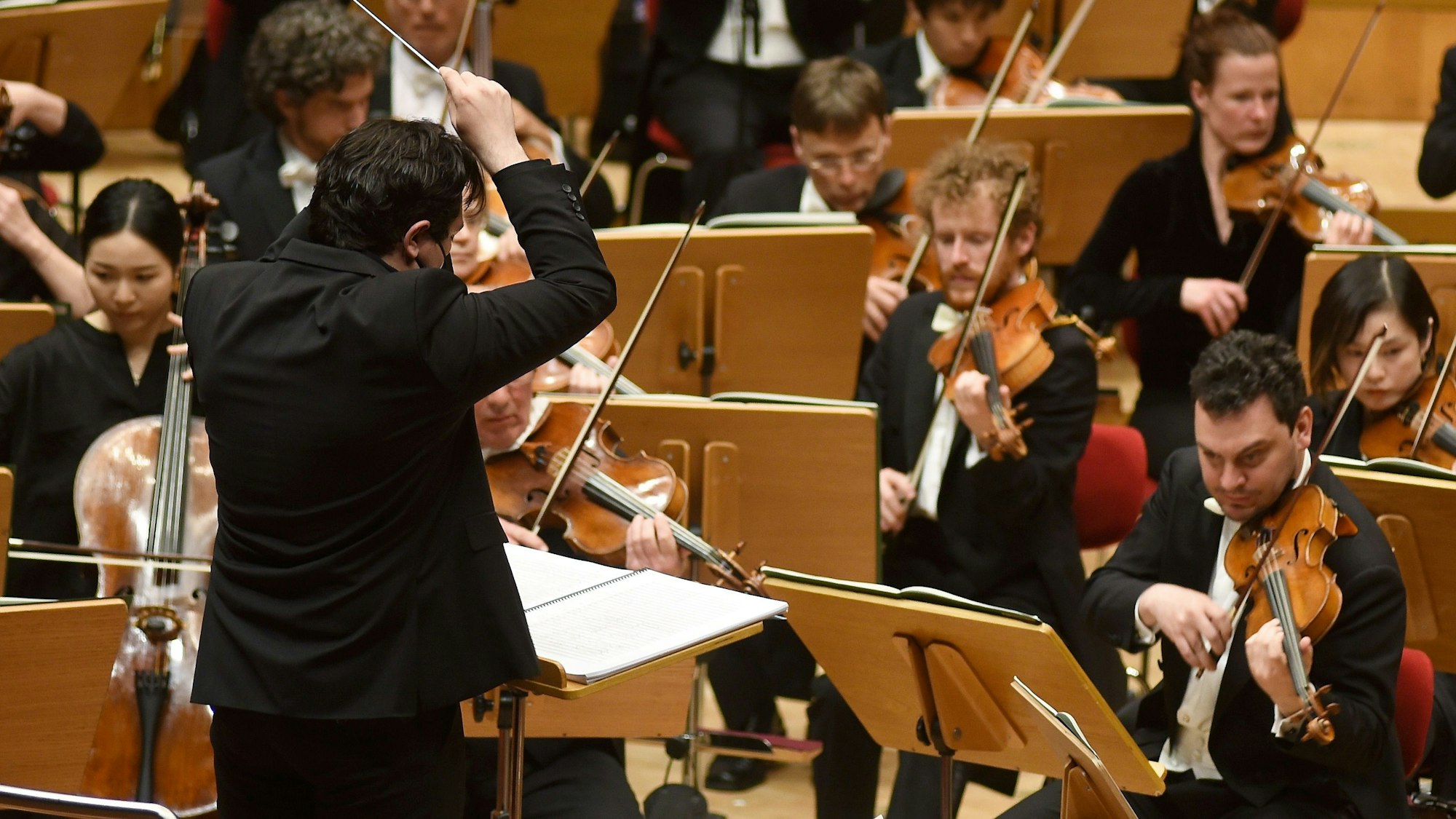 Chef-Dirigent Cristian Macelaru steht mit dem Rücken zu uns vor den Streichern des Orchesters.