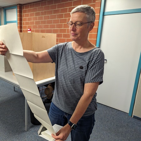 Auf dem Foto ist eine Frau zu sehen, die den Stimmzettel betrachtet.