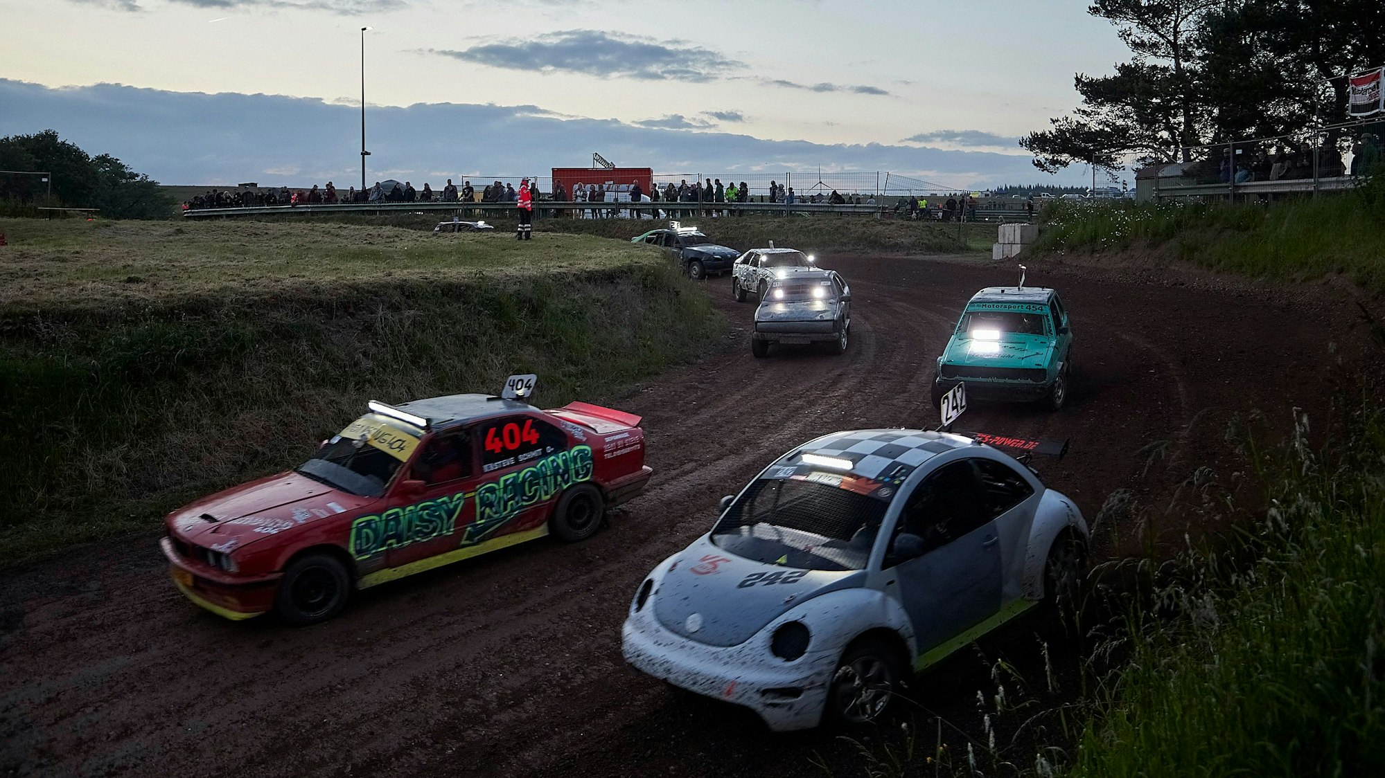 Mehrere Rennautos fahren in der Dämmerung über eine Erdstrecke.