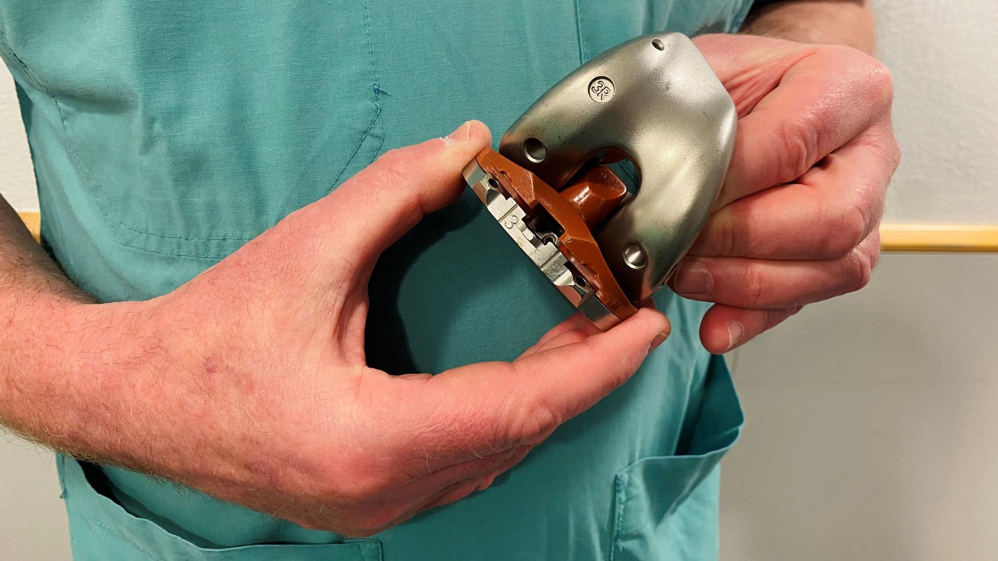 Ein Arzt hält eine Knieprothese in der Hand.
