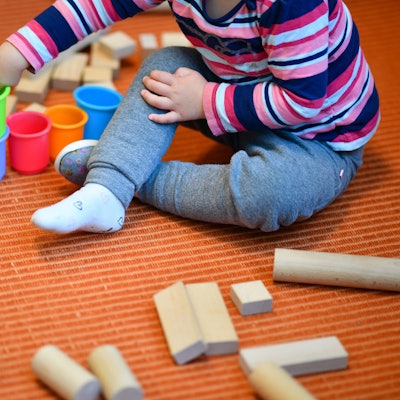 Ein Mädchen spielt in einer Kita mit bunten Bechern und Bauklötzen.