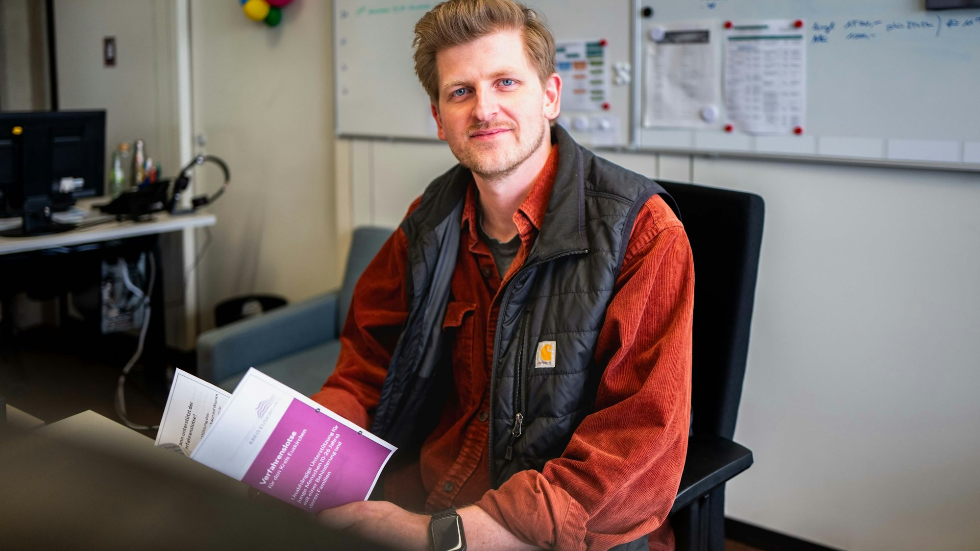 Das Bild zeigt Timo Laas, wie er am Schreibtisch sitzt. In der Hand hält er einen Flyer.