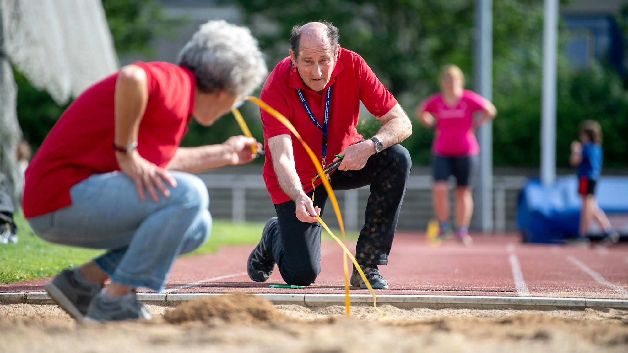 Zwei Sportabzeichenprüfer nehmen in der Weitsprunggrube mit einem Band Maß.
