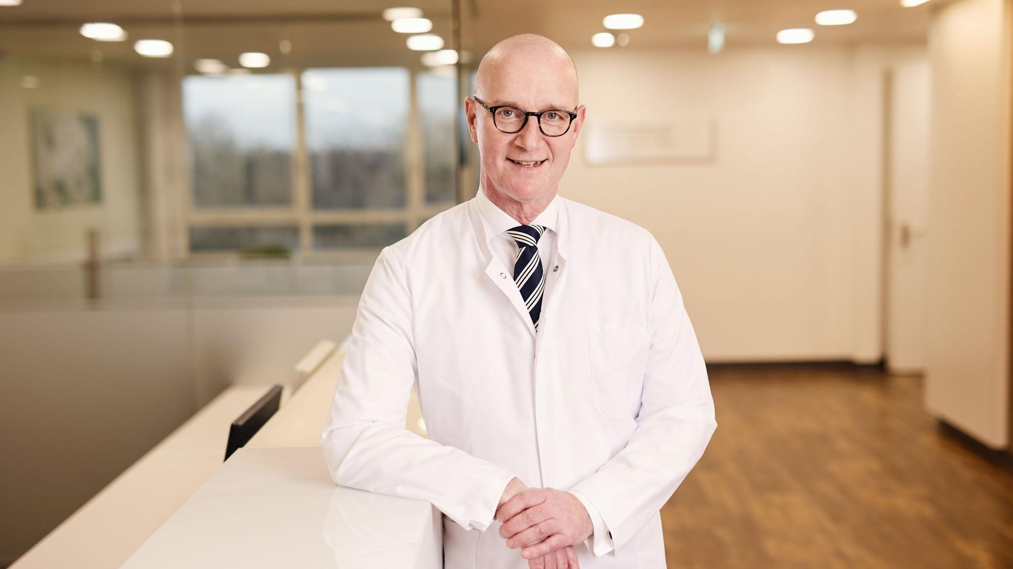 Leonard Bastian, Chefarzt der Klinik für Orthopädie und Unfallchirurgie, steht angelehnt an einem Empfangstresen im Klinikum Leverkusen.