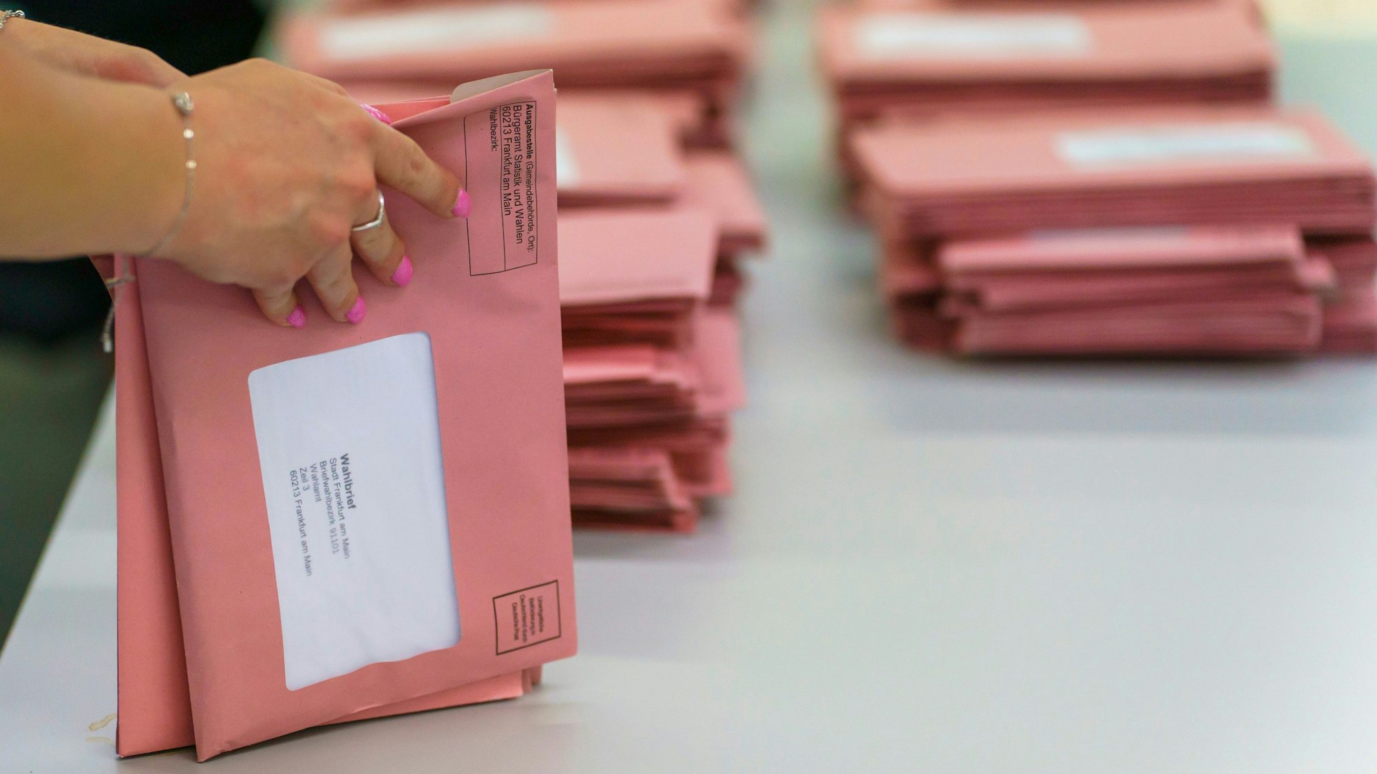 Eine Frau sortiert rote Briefwahlumschläge.
