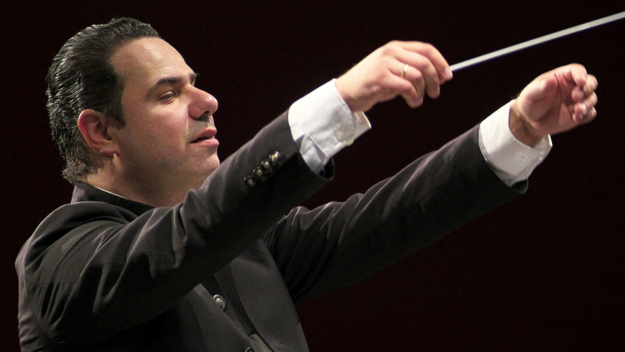 Ein Mann hebt die Arme und dirigiert mit einem Stab.