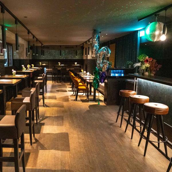 Zu sehen ist eine Bar von innen, mit Tischen und Stühlen.
