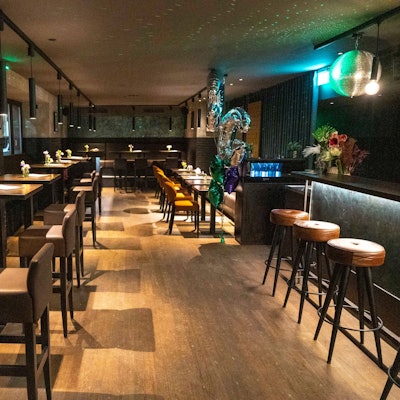 Zu sehen ist eine Bar von innen, mit Tischen und Stühlen.
