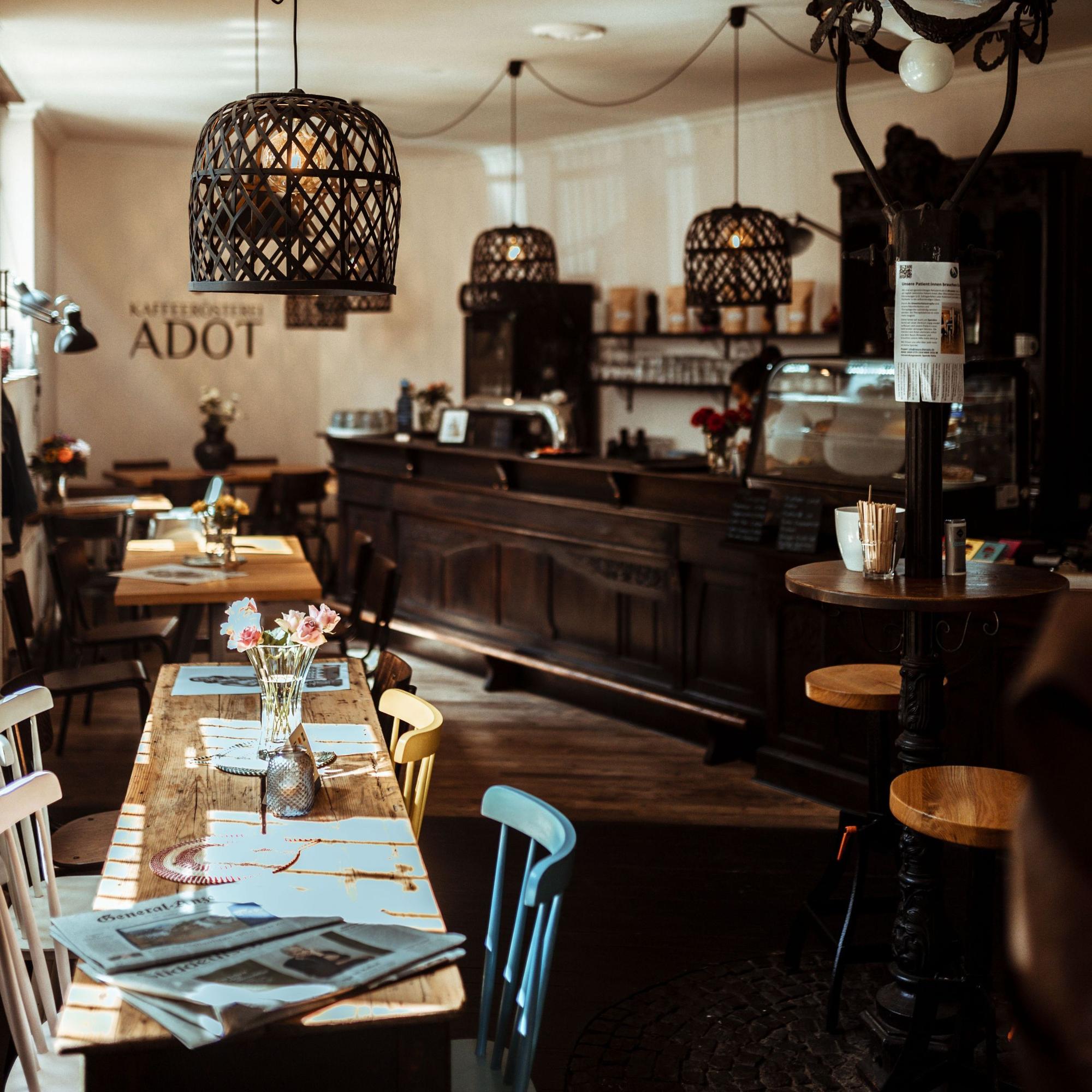 Die Innenansicht des Cafés Adot. Auf der linken Seite Stühle und Tische. Rechts eine Straßenlaterne, weiter hinten rechts eine Theke.