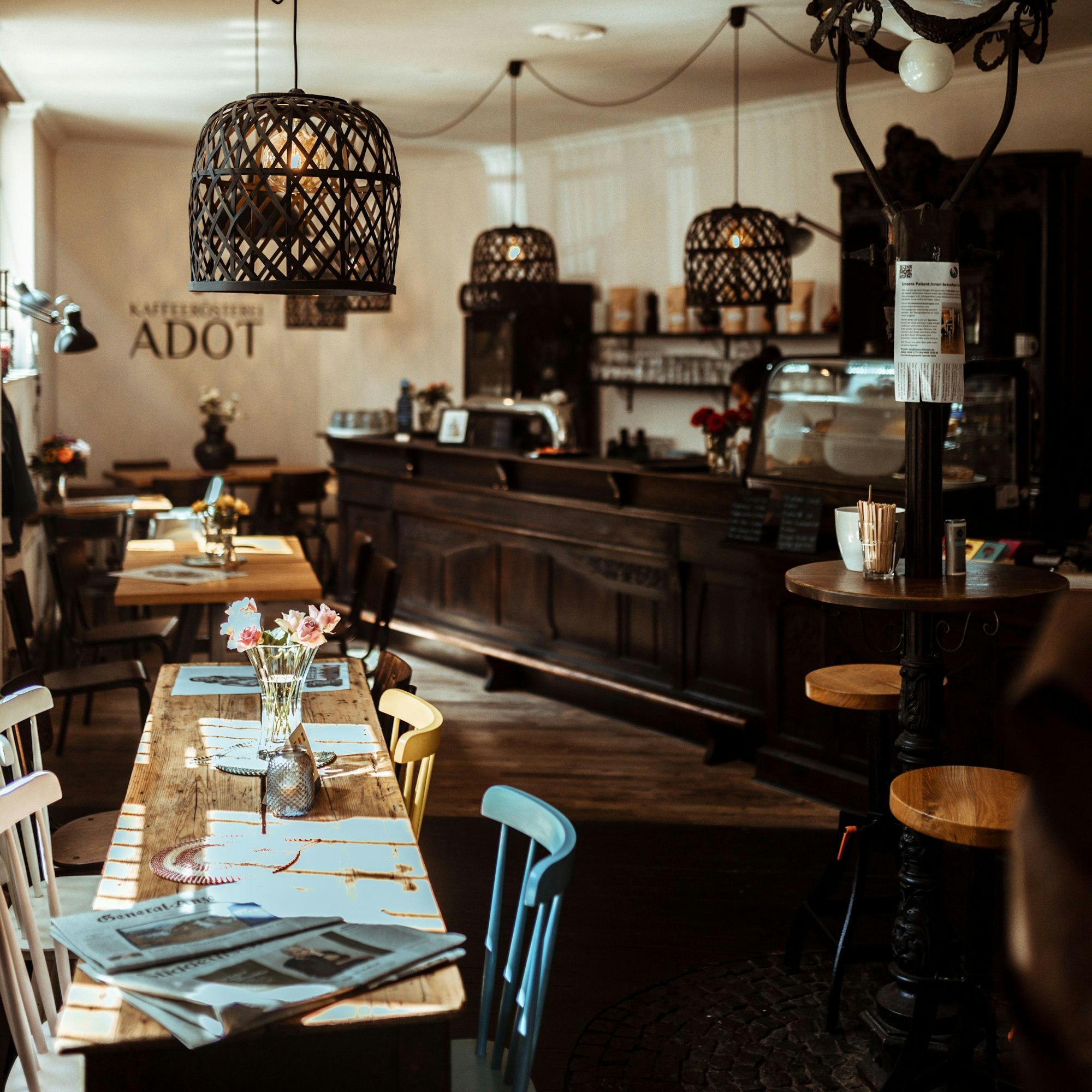 Die Innenansicht des Cafés Adot. Auf der linken Seite Stühle und Tische. Rechts eine Straßenlaterne, weiter hinten rechts eine Theke.