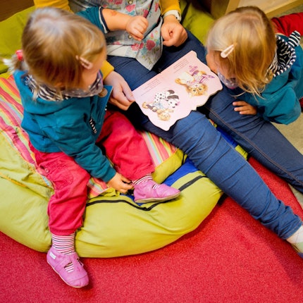 Eine Erzieherin liest mit Zwillingen ein Buch. (Symbolbild)