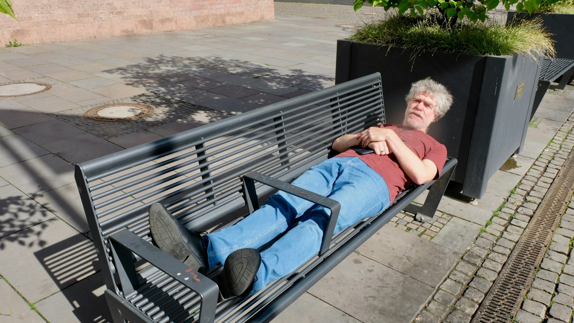 Zu sehen ist ein Mann, der auf einer Bank liegt.