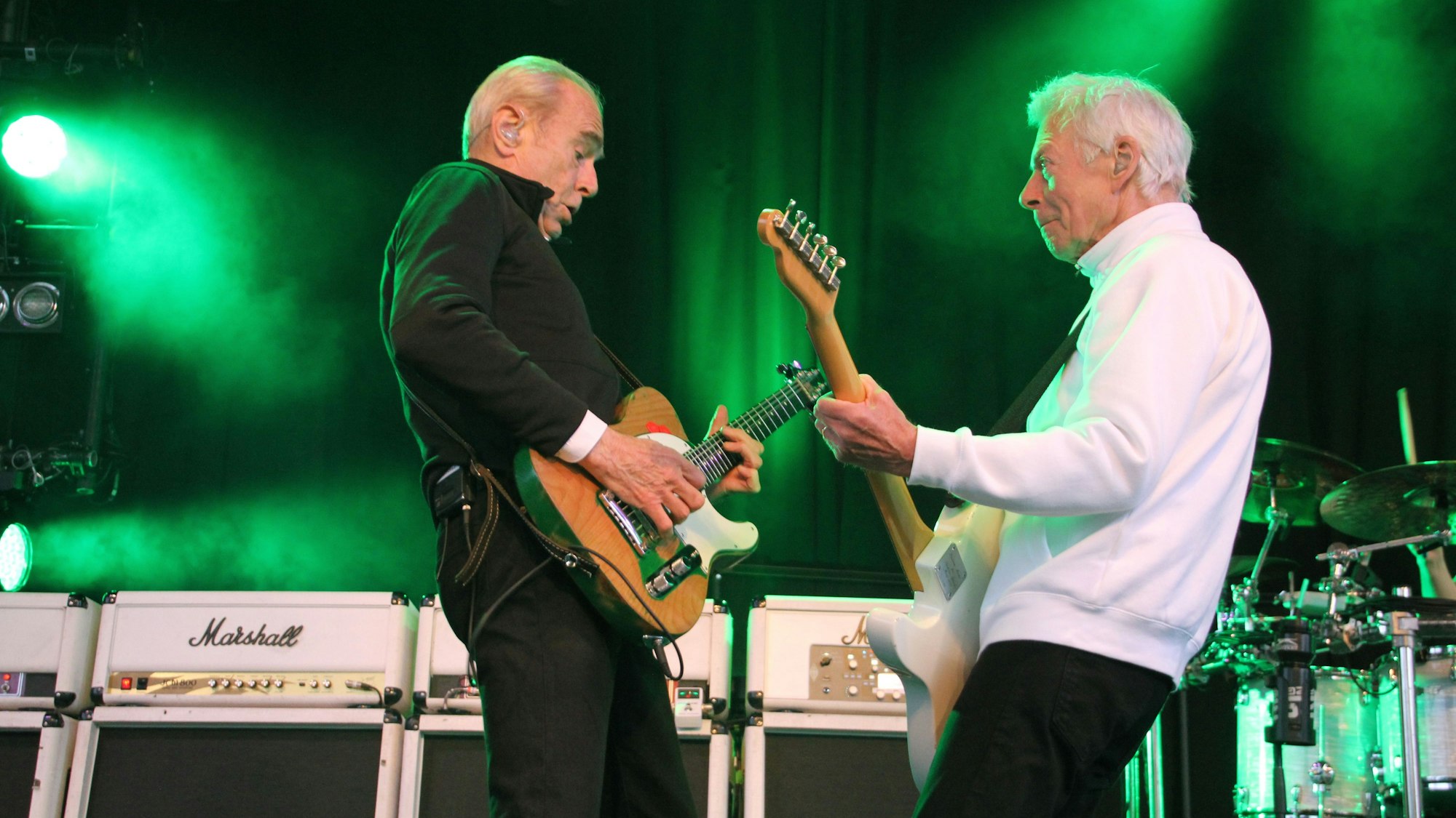 Francis Rossi und Andy Brown von Status Quo spielen Gitarre. Sie stehen sich gegenüber, mit leicht nach hinten gebogenen Oberkörpern.