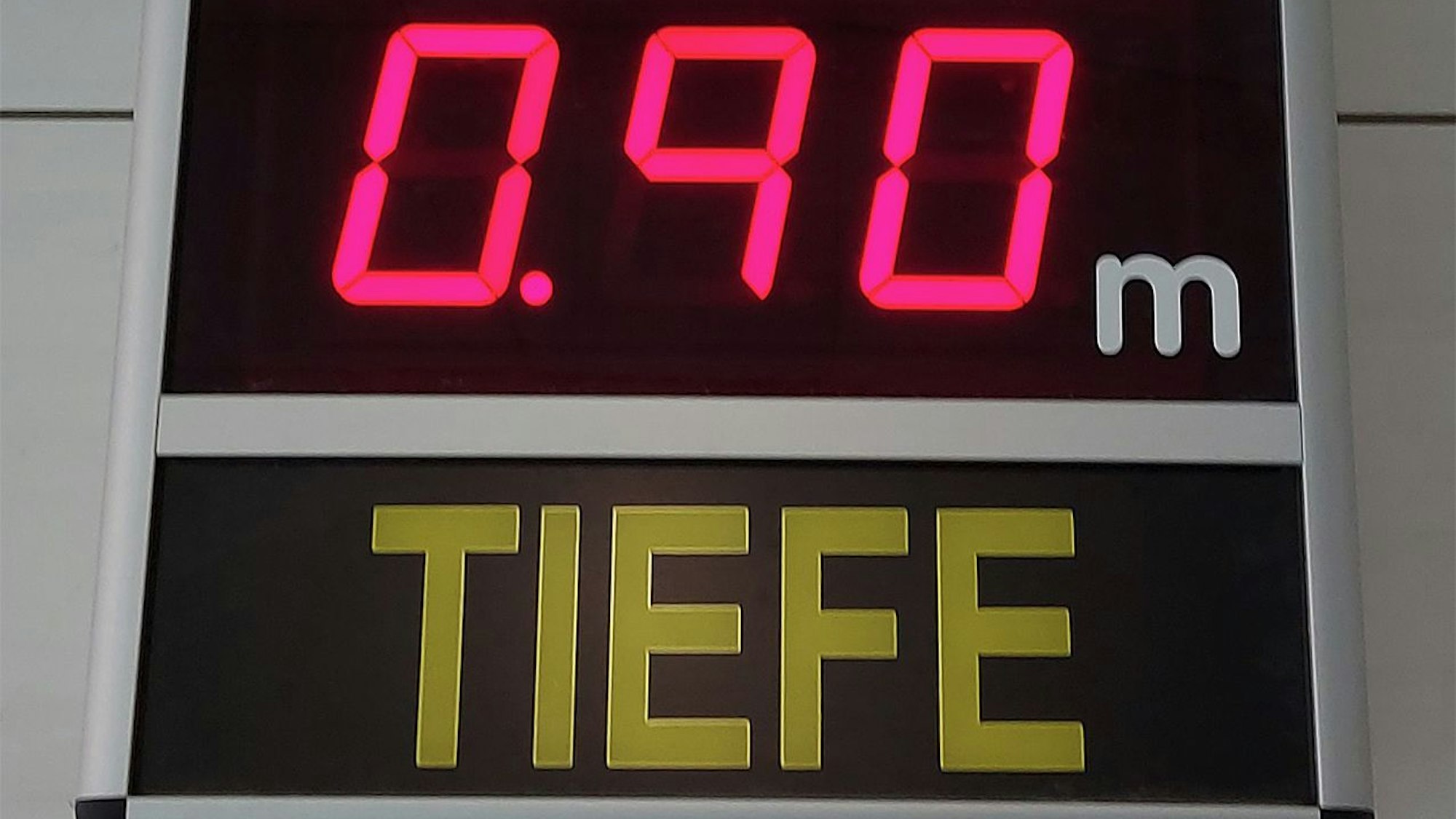 Eine elektronische Anzeige zeigt in roten Ziffern eine Wassertiefe von 0,90 Metern im Hallenbad an.