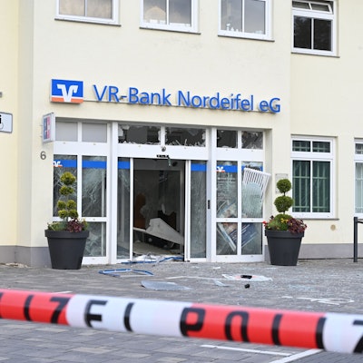 In Dahlem haben Unbekannte versucht, den Geldautomat der VR-Bank zu sprengen. Vor dem Gebäude mit dem blauen Schriftzug der Bank liegen Splitter, ein rot-weißes Band mit der Aufschrift Polizei sperrt den Tatort ab.