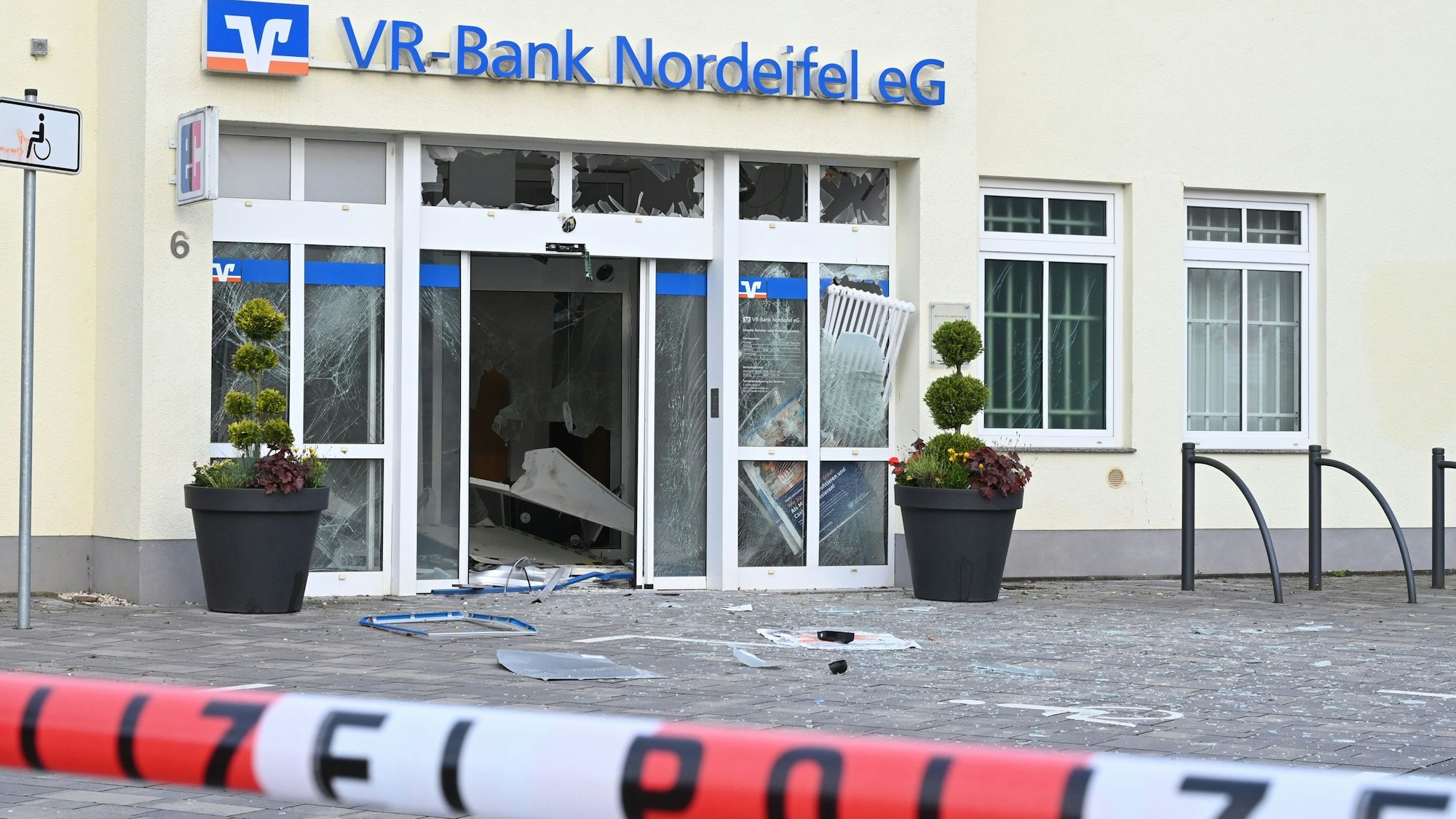 In Dahlem haben Unbekannte versucht, den Geldautomat der VR-Bank zu sprengen. Vor dem Gebäude mit dem blauen Schriftzug der Bank liegen Splitter, ein rot-weißes Band mit der Aufschrift Polizei sperrt den Tatort ab.