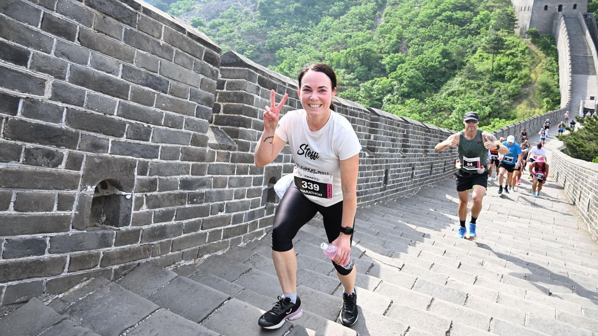 Stefanie Bart steht auf der Chinesischen Mauer und macht mit zwei Fingern das „Peace-Zeichen“.