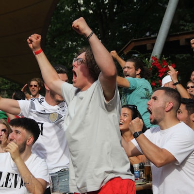 Menschen, zum Teil in Trikots, springen in die Höhe und jubeln.