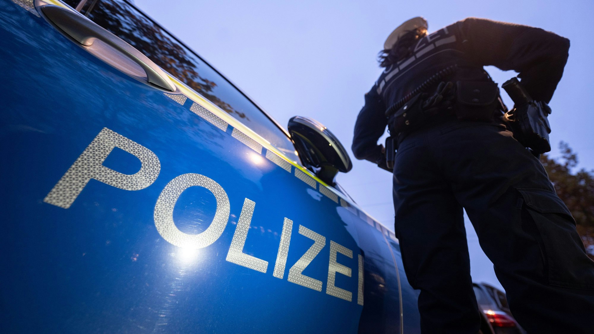 Eine Polizistin steht neben einem Polizeifahrzeug.