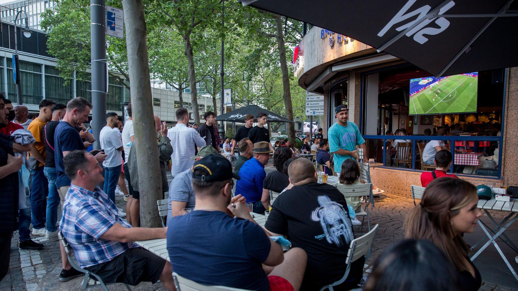 Viele Menschen sitzen vor der Joe Champs Bar und schauen gemeinsam Fußball.
