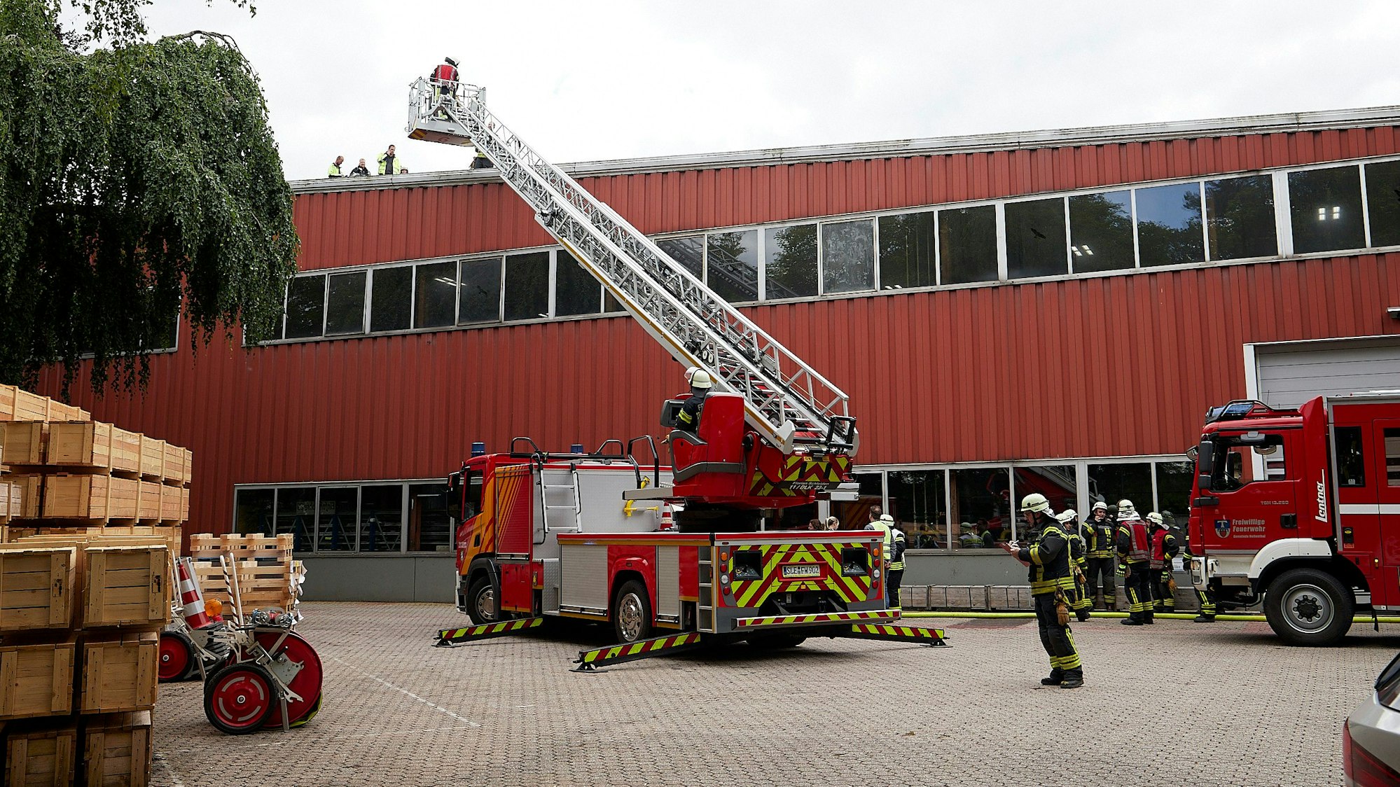 Vor einer Werkshalle mit roter Front hat die Feuerwehr die Drehleiter ausgefahren.