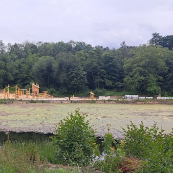Das Foto zeigt den Heilteich und im Hintergrund den neuen Pavillon und den Spielplatz.