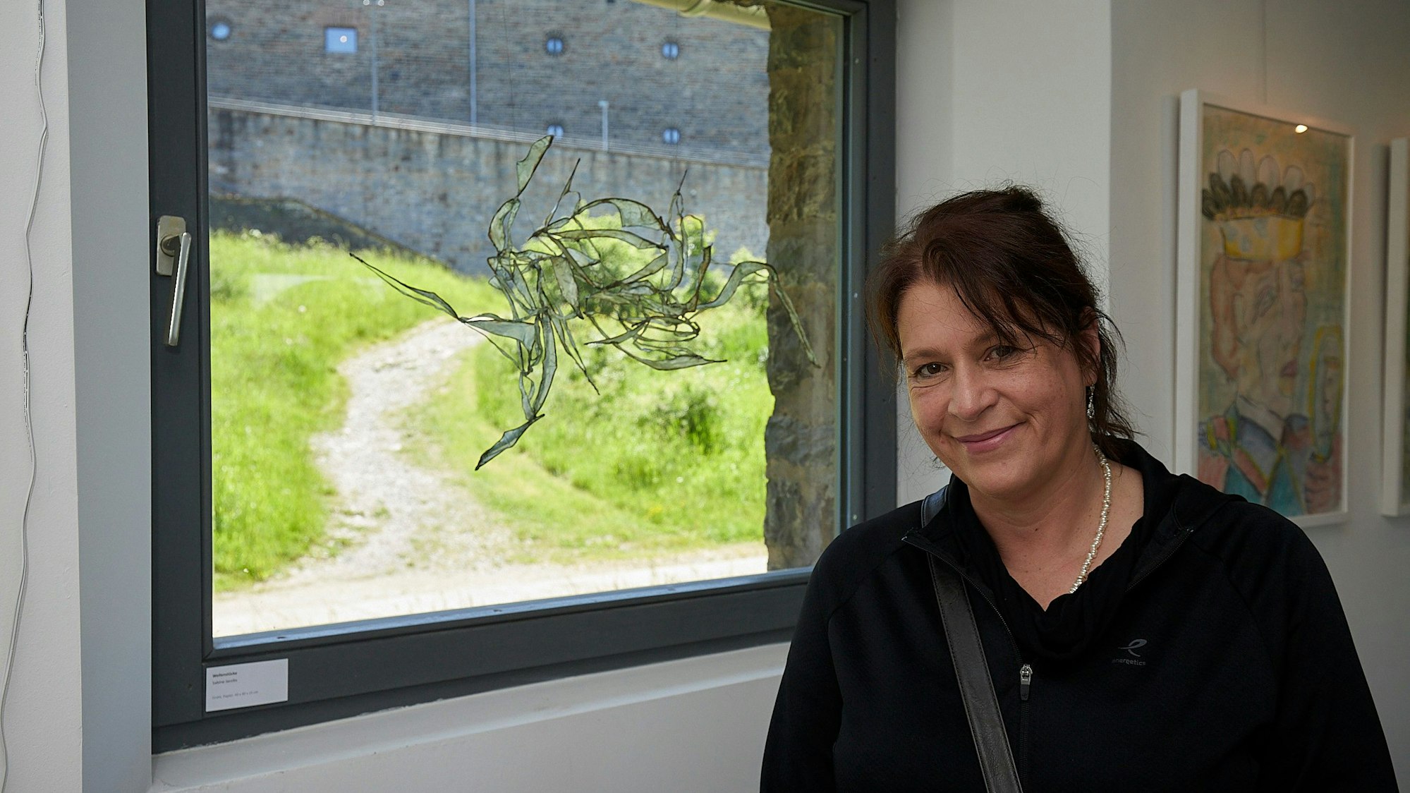 Sabine Jacobs steht neben einem Fenster, vor dem ein Kunstwerk hängt.
