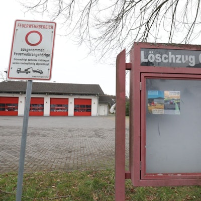Ein leerer Schaukasten mit der Aufschrift Löschzug Oelberg, im Hintergrund das Gerätehaus mit vier roten Rolltoren.