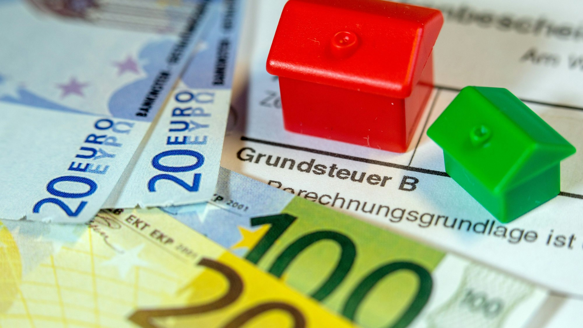 Ein Spielzeughaus und die Nachbildung von Euro-Geldscheinen liegen auf einem Abgabenbescheid für die Entrichtung der Grundsteuer.