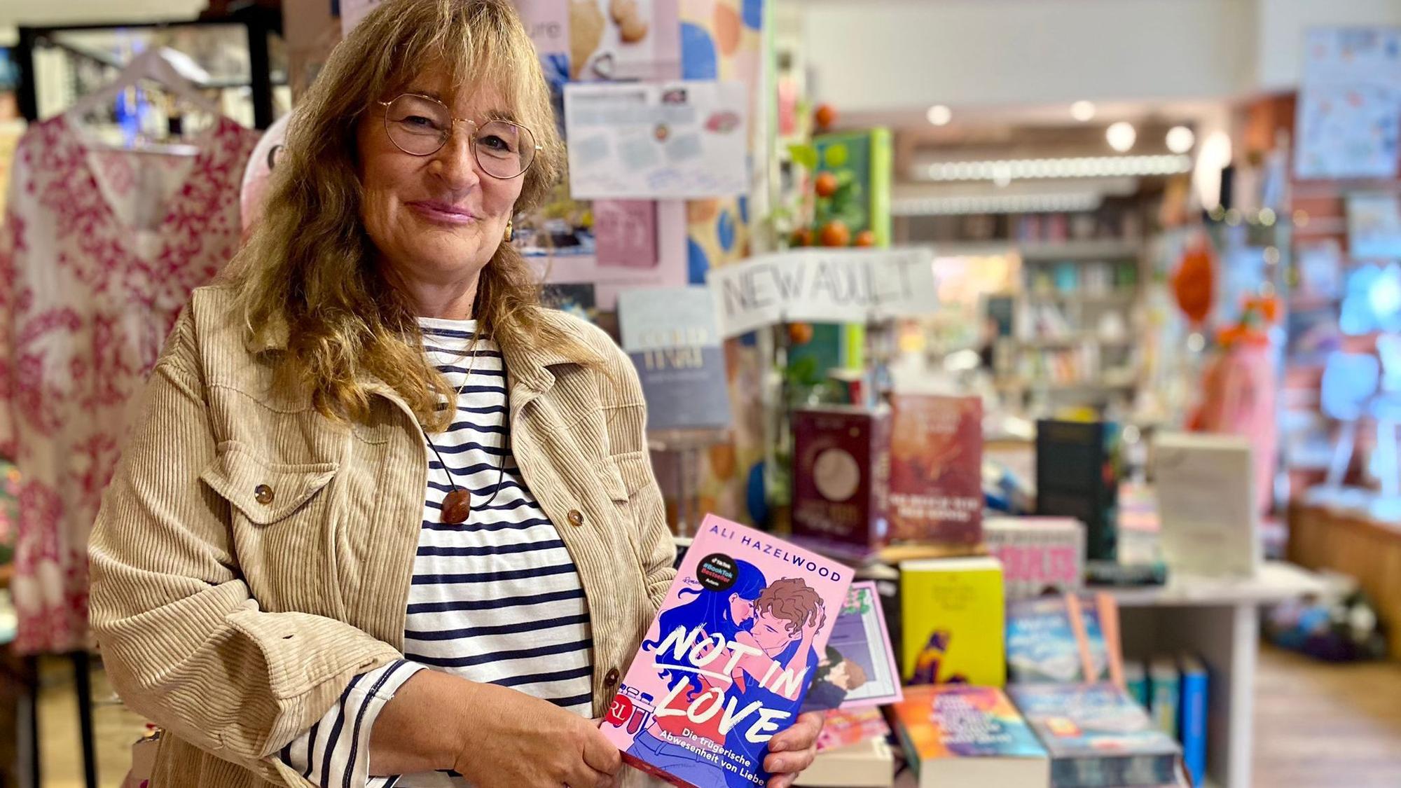 Renate Elsen steht in der Bücherecke in Blankenheim und präsentiert das Buch „Not in Love“ von Ali Hazelwood.