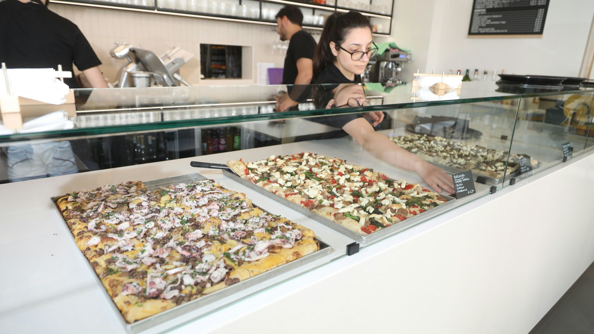 verschiedene Sorten Focaccia werden von einer Mitarbeiterin in eine Theke einsortiert